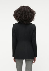 Musta bleiseri rakenteellisella suunnittelulla, yksinkertainen ilmanventtiili ja pitkät hihat. Teksturoitu hiilenharmaa haukansilmäkuosiset housut.