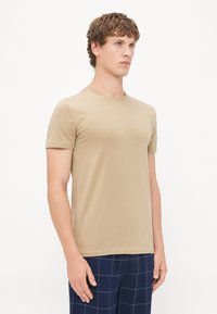 Tricou bej cu mânecă scurtă și guler circular, realizat dintr-un material neted. Tricoul se asează strâns pe corp și are un design curat și minimalist.