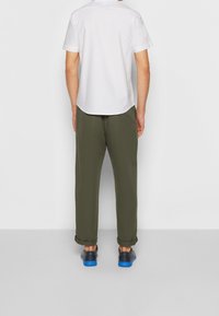 Vit kortärmad skjorta, olivgröna byxor och svarta skor med blå sulor. Enkel design, slät struktur och avslappnad passform.