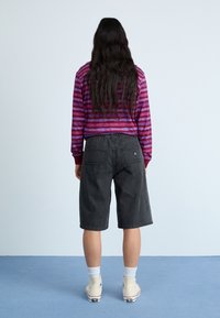 Top de manga larga a rayas púrpura y rosa con puños rojos, combinado con pantalones cortos de mezclilla grises. La modelo lleva calcetas blancas y zapatillas altas beige.