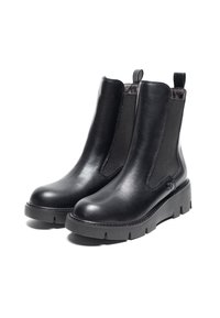 Botas de tobillo de cuero negro con paneles laterales elásticos, suela de goma plana y tiradores. Textura suave con detalles de costura.