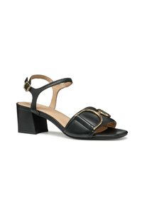 Sandalias de tacón de cuero negro con una amplia correa frontal, textura acolchada, detalle de hebilla en tono dorado y diseño de tacón cuadrado.