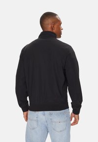 Giubbotto bomber nero con colletto alto, polsini elasticizzati e orlo a costine. Realizzato in tessuto liscio, presenta un design pulito senza motivi visibili.