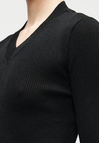 Camisola preta em malha canelada com decote em V. Vista aproximada que mostra a textura e o ajuste ao redor dos ombros e do decote. Design suave e justo.