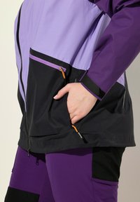 Lila och svart vattentät jacka med blixtlås, fickor och kardborre cuffs. Har en blandning av matta och blanka texturer.