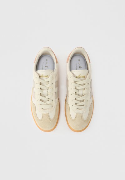 Μπεζ αθλητικά παπούτσια χαμηλού προφίλ με υφή από σουέντ στην περιοχή των δαχτύλων, λείες δερμάτινες πλευρές, ελαστικά κορδόνια και ταμπά λαστιχένια σόλα. Χρυσή λεπτομέρεια με το λογότυπο στη γλώσσα.