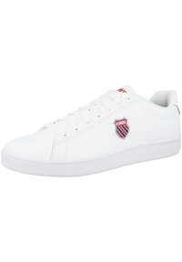 White sneaker with a smooth synthetic upper, round toe, lace-up closure, and a shield logo on the side. Features a textured rubber sole.
