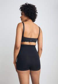 Svart blondet bralette med bølgete kanter og justerbare stropper; matchende høytlivte shorts i et glatt, elastisk materiale.