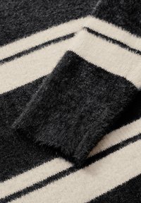 Gros plan sur un pull noir et crème à rayures, présentant une texture douce et duveteuse avec un poignet côtelé et des lignes horizontales contrastées.