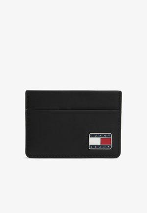 Portacarte nero slim con due fessure per le carte e una piccola patch con il logo Tommy Jeans in rosso, bianco e blu nella parte anteriore in basso a destra.