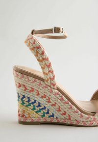 Sandale compensée avec talon en jute tressé multicolore et bride, bride à la cheville beige avec boucle, et semelle en cuir marron clair.