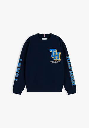 Sweat-shirt bleu marine à col rond avec de grandes lettres "TH" bleues et jaunes et logo Tommy Hilfiger sur le devant et les manches.