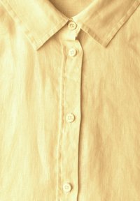 Camicia di lino giallo chiaro con colletto button-down, dotata di cinque bottoni sul davanti e una superficie in tessuto texturizzato.