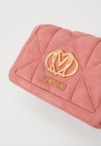 Rozā kvadrātveida zamšādas sajūgs soma ar zelta toņu Love Moschino logotipu. Dizains ietver šūtas dimanta formas rakstus un noapaļotas malas.