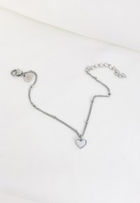 Collar de cadena de plata que presenta un colgante en forma de corazón pulido, con un cierre de langosta y una cadena de extensión ajustable. Diseño simple y textura suave.