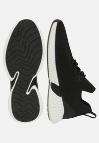 Svarta sportskor med en stickad ovandel, utrustade med en texturerad vit sula och elastiska snören. Sidokapningar ger en modern designkomponent.