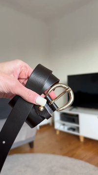 Zwarte leren riem met een glanzende, goudkleurige gesp en studdetail, omhoog gehouden om de gladde textuur en het ontwerp te benadrukken.