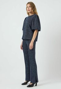 Completo in due pezzi blu navy con tessuto testurizzato. La parte superiore ha maniche corte a sbuffo, mentre i pantaloni presentano slits laterali e una linea dritta. Scarpe nere.