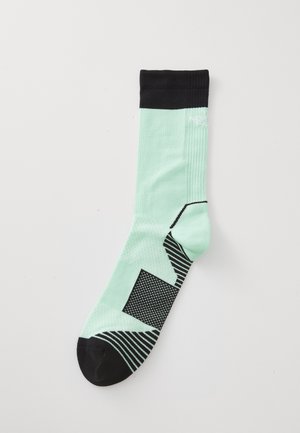 Mintgrønne sokker med sort ribbet mansjett, mønstrede detaljer og strukturerte teksturer. Har svart tå og geometriske designelementer.