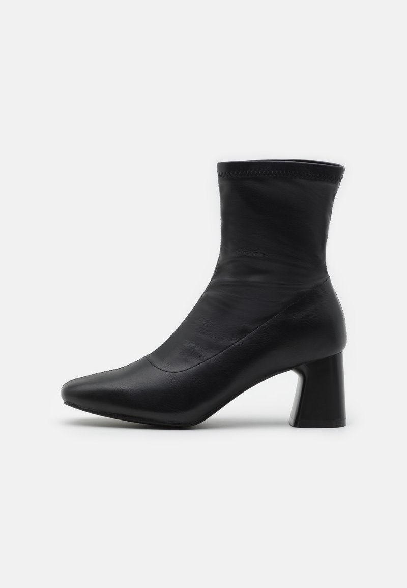 Botte noire en cuir mi-mollet avec un bout pointu et un talon bloc sur un fond blanc uni.