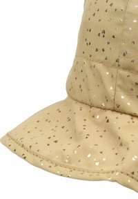 Chapeau seau beige en tissu doux, avec un motif de cœurs dorés brillants, un large bord et des coutures le long des bords.