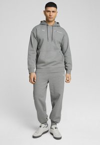 Siv hoodie in trenirka, izdelana iz mehkega materiala. Ima sprednje žepe, elastične manšete in subtilne logotipne detajle.