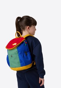 Krāsaina mugursoma ar zilām, zaļām un sarkanām panelēm un dzelteniem akcentiem. Mīksts, teksturēts vāks ar logotipu. Regulas siksnas un sānu kabata.