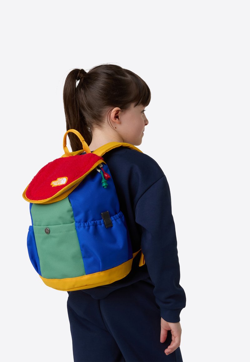 Krāsaina mugursoma ar zilām, zaļām un sarkanām panelēm un dzelteniem akcentiem. Mīksts, teksturēts vāks ar logotipu. Regulas siksnas un sānu kabata.