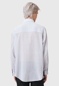 Bijela, lagana košulja dugih rukava od teksturirane tkanine s suptilnim prugastim uzorkom, s klasičnom kragnom i manžetama na dugmad.