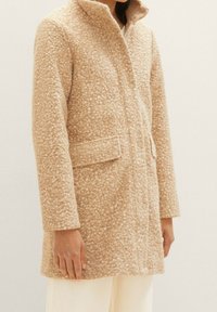 Beige ullrock med en strukturerad, fläckig mönstring, med krage, framknappar och sidofickor. Enkel, rak skärning.