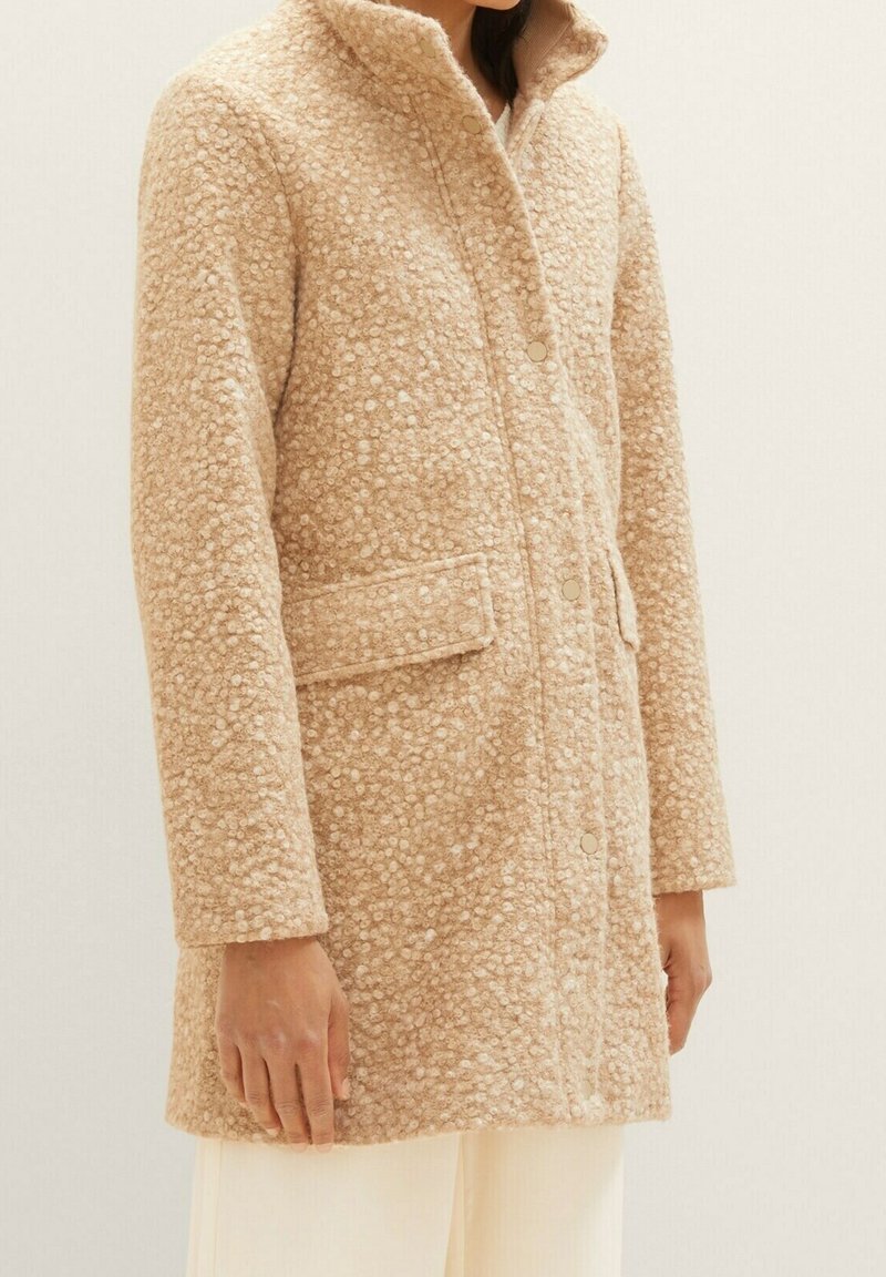 Beige ullrock med en strukturerad, fläckig mönstring, med krage, framknappar och sidofickor. Enkel, rak skärning.