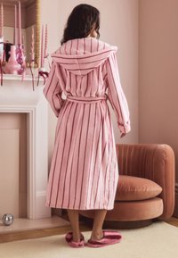 Pink striped bathrobe with a hood, soft texture, and a tied waist. Cozy slippers in matching pink complete the look in a softly lit setting.