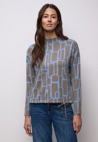 Top de manga larga con estampado marrón y azul, con cuello alto y detalle de cordón en el dobladillo, combinado con jeans azules.