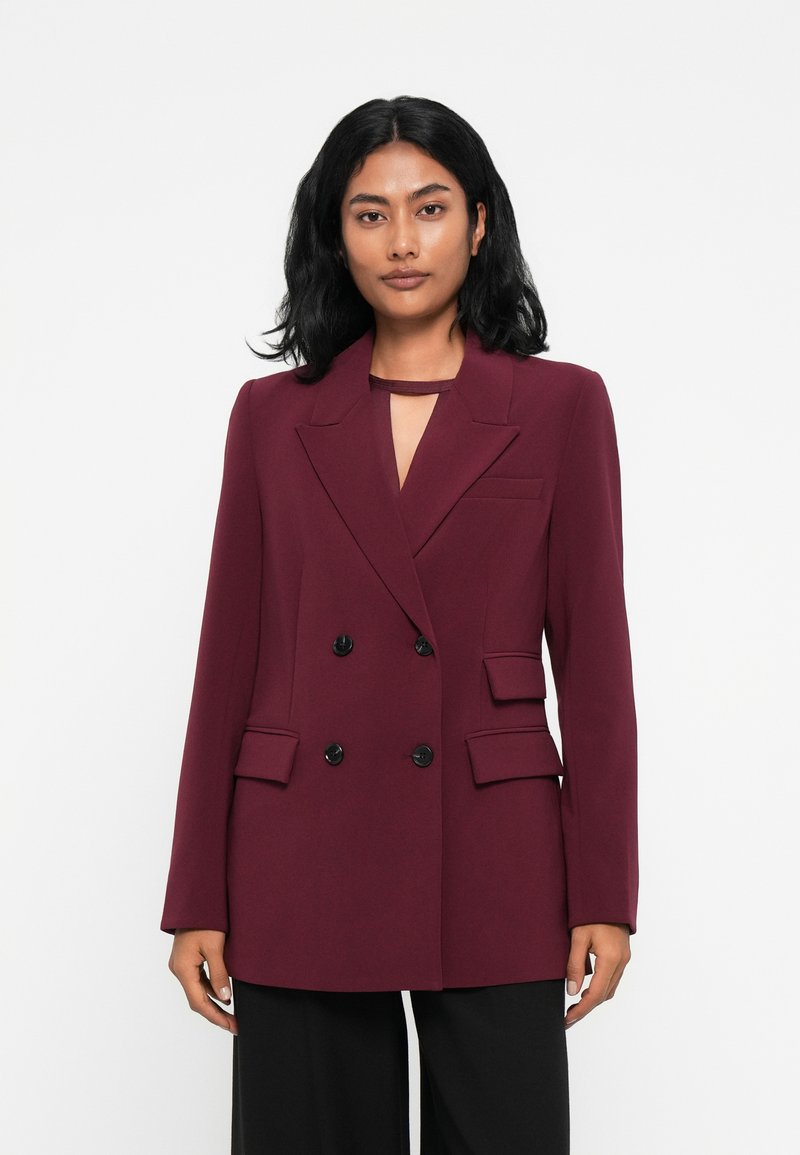 Blazer bordeaux de duas fileiras de botões com lapelas recortadas, bolsos laterais e detalhe de decote em forma de buraco de chave; tecido suave com um corte ajustado.
