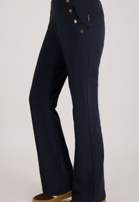 Marineblauwe broek met een uitlopende stijl, voorzien van goudkleurige knopen, een gestructureerde tailleband en een zijzak voor een functioneel detail.