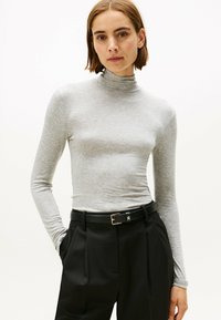 Grauer langärmeliger Rollkragenpullover aus glattem Stoff, kombiniert mit hochtaillierten schwarzen Hosen, die mit einem Gürtel mit metallischer Schnalle versehen sind.