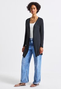 Cárdigan negro de manga larga con un frente abierto. Combinado con unos vaqueros de pierna ancha en un azul claro y sandalias mínimas de tiras. Textura suave, ajuste relajado.