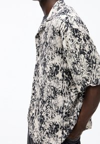 Camicia a maniche corte con stampa astratta in bianco e nero. Realizzata in tessuto leggero con chiusura davanti a bottoni e una vestibilità rilassata.