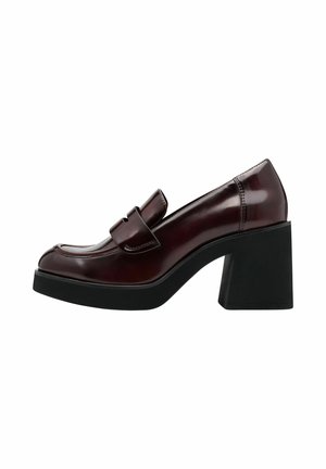 Zapato tipo mocasín de charol burdeos con punta redonda, una correa decorativa y un tacón negro grueso. Textura suave.