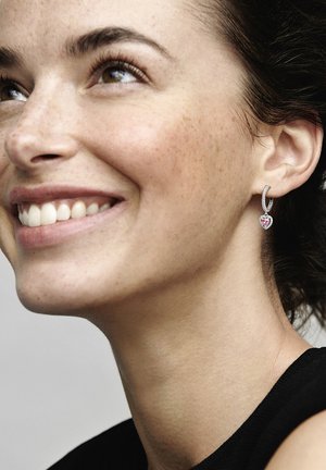 Orecchino a cerchio in argento con una pietra preziosa rosa a forma di cuore e accenti in zirconia cubica, presentato su uno sfondo neutro.