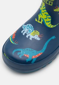 Marine gummistøvel med fargeglade dinosaurillustrasjoner i nyanser av grønn, blå og rød på den øverste overflaten. Jevn tekstur.