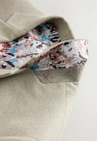 Bolso de tela beige con un forro de estampado floral en colores pastel, con una textura suave y sutiles acentos de fieltro en la abertura.