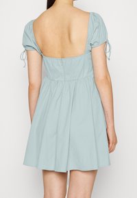 Ljusblå klänning med korta puffärmar, djup fyrkantig rygg, dragkedjestängning och ett lätt texturerat tyg. Utsvängt kjoldesign.