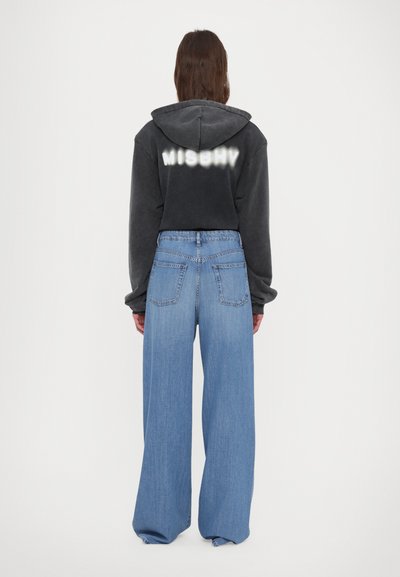 Abgeschnittenes schwarzes Hoodie mit "MISBHY"-Text auf dem Rücken, kombiniert mit lockerer, hellblauer Jeans. Strukturiertes Material und weit geschnittenes Design.