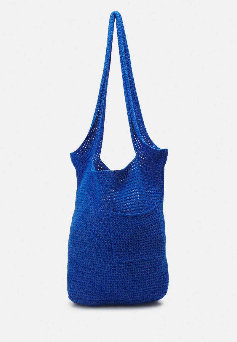 Sac d'épaule crocheté bleu vif avec une poche avant et de longues bretelles, présenté sur un fond blanc uni.