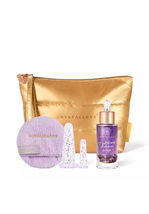 Złota kosmetyczna torebka z fioletową butelką serum z połyskiem, dwoma przezroczystymi aplikatorami i lawendową podkładką do oczyszczania z napisem CRYSTALLOVE.