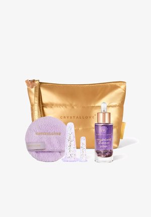 Trousse cosmétique dorée avec un flacon de sérum scintillant violet, deux applicateurs transparents et un tampon de nettoyage lavande portant le label CRYSTALLOVE.