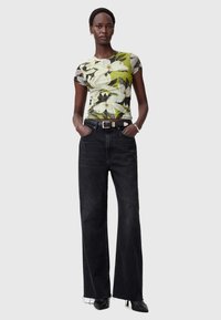 Blomstermønstret t-shirt med korte ærmer i grøn og hvid, parret med højtaljede sorte vidde jeans og sorte højhælede sko.