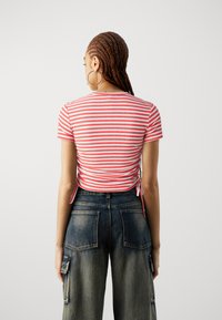 Rød og hvitstripet kortermet topp med rynket bak, kombinert med høyt liv mørk denim cargo bukser med synlige sømmer og lommer.