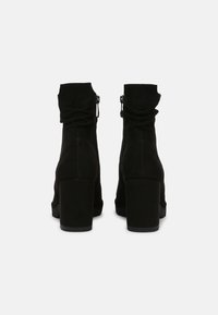 Bottines en suède noir avec un talon empilé, fermeture éclair sur le côté et un haut légèrement froncé pour un fit décontracté.
